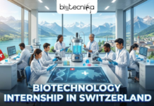Biotechnology Internship in Switzerland | Merck Offers Internship Opportunity for Life Science Students Biotechnology Internship in Switzerland Merck Offers Internship Opportunity for Life Science Students. A featured image with the Biotecnika Global logo centered at the top. The scene showcases a futuristic biotechnology laboratory nestled against a backdrop of the majestic, snow-capped Swiss Alps visible through a wide window. Inside the lab, a diverse team of scientists is collaborating on advanced research, with one researcher holding a test tube reflecting the clear blue sky. High-tech equipment like bioreactors and glowing digital displays of DNA sequences fill the room. Across the bottom, bold text reads "BIOTECHNOLOGY INTERNSHIP IN SWITZERLAND" in a clean white font with a vibrant red and white border, echoing the colors of the Swiss flag.