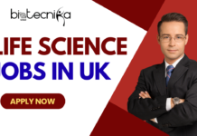 Life Science Jobs in UK | Sanofi Hiring For Associate Medical Advisor A promotional banner for Biotecnika Global, featuring the large text 'LIFE SCIENCE JOBS IN UK' in red and blue. On the right, a man in a black pinstripe suit and blue tie stands with crossed arms, against a background split between white and red with a Union Jack flag graphic. Below the text is a red button with 'APPLY NOW'."
