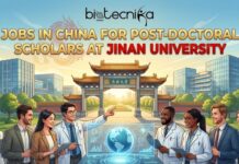 Explore Post-doctoral Scholar Opportunity at Jinan University Post doctoral Scholar Opportunity In China | Apply Now. An illustrative image with the black and white "Biotecnika Global" logo at the top center. Below it, large gold text reads "JOBS IN CHINA FOR POST-DOCTORAL SCHOLARS AT" with "JINAN UNIVERSITY" in prominent red capital letters. A diverse group of eight smiling professionals, some in lab coats and others in business suits, stands in front of the traditional Chinese gate of Jinan University. One man in a lab coat points to a futuristic, glowing holographic display showing a globe and data. The background features modern university buildings under a blue sky with a subtle, translucent golden dragon illustration in the upper left. The overall style is a colorful digital illustration.