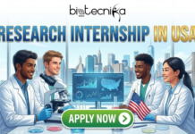 Explore Research Internships in USA | Sartorius USA Hiring Today Research Internship in USA Life Science Internship at Sartorius USA. A featured image with the title "RESEARCH INTERNSHIP IN USA" in large blue text at the top. Below it, the Biotecnika Global logo is visible. The main illustration shows four diverse researchers—two men and two women—in a modern laboratory setting, wearing lab coats. They are gathered around a desk with a microscope, petri dishes, a small American flag, and a computer screen displaying charts and a map of the USA. The background features a large window with a panoramic view of the New York City skyline, including the Statue of Liberty and the Brooklyn Bridge. At the bottom center, there is a large green button with white text that reads "APPLY NOW"