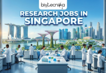 Research Jobs in Singapore at Genome Institute of Singapore | Opportunity You Can’t Miss Research Jobs in Singapore at Genome Institute of Singapore. A featured image with the Biotecnika Global logo centered at the top. The image depicts a state-of-the-art laboratory in Singapore, where a diverse group of researchers is working with advanced genomic sequencing equipment. Through a large window in the background, the iconic Singapore skyline is visible, featuring landmarks like the Marina Bay Sands and the Supertree Grove at Gardens by the Bay. A digital screen in the lab displays a DNA helix and a map of Singapore. Across the bottom, bold text reads "RESEARCH JOBS IN SINGAPORE" in a white font with a sleek blue and silver border.