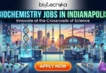Biochemistry Jobs in Indianapolis | Eurofins Hiring For Analytical Biochemist Role Biochemistry Jobs in Indianapolis | Eurofins Hiring For Biochemist. A professional featured image titled "BIOCHEMISTRY JOBS IN INDIANAPOLIS" with the tagline "Innovate at the Crossroads of Science." The illustration depicts a modern biochemistry laboratory with a diverse team of scientists working with microscopes, digital monitors, and colorful chemical solutions. A large window in the background provides a view of the Indianapolis skyline, featuring the Soldiers and Sailors Monument and the Lucas Oil Stadium at sunset. A prominent orange "APPLY NOW" button is at the bottom.