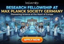 Research Fellowship at Max Planck Society | Latest Life Science Opportunity in Germany Research Fellowship at Max Planck Society Germany | Apply Now. A promotional graphic from Biotecnika Global titled "RESEARCH FELLOWSHIP AT MAX PLANCK SOCIETY GERMANY" with the subtitle "Pioneering Science at the Heart of Europe." The illustration shows a diverse group of scientists working in a futuristic laboratory filled with advanced equipment, holographic displays of molecules, and screens showing atomic structures and galaxies. Through large panoramic windows in the background, the Brandenburg Gate and a German flag are visible. A prominent orange "APPLY NOW" button is at the bottom.