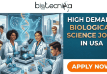 High-Demand Biological Science Jobs in USA | Join AbbVie Today!! High-Demand Biological Science Jobs in USA Join AbbVie. A promotional graphic from Biotecnika Global advertising "High Demand Biological Science Jobs in USA." The image features an AI-generated illustration of a diverse team of five scientists in white lab coats and blue gloves working in a high-tech laboratory. The lab is equipped with a microscope, pipettes, and digital tablets, with a large glowing DNA double helix in the center. A large window in the background shows a city skyline including the Empire State Building. The right side of the graphic displays bold text with the job headline and a prominent orange "APPLY NOW" button.