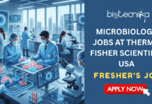 High-Demand Fresher’s Microbiology Jobs in USA | Thermo Fisher Scientific Hiring Now High-Demand Fresher's Microbiology Jobs in USA Thermo Fisher Scientific Hiring Now. A professional job recruitment banner for Biotecnika Global. The left side features a high-tech microbiology laboratory where scientists in blue scrubs and protective gear work with glowing petri dishes, microscopes, and digital monitors showing viral structures. The right side has a dark blue background with the Biotecnika Global logo at the top, bold white text reading "MICROBIOLOGY JOBS AT THERMO FISHER SCIENTIFIC USA," a tagline "Innovate & Impact Global Health – Explore Your Future," and a vibrant orange "APPLY NOW" button at the bottom.