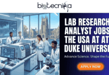 High-Impact Lab Research Analyst Jobs in the USA at Duke University | Apply Today High-Impact Lab Research Analyst Jobs in the USA at Duke University Apply Today. A featured image for a job posting with the "biotecnika Global" logo at the top. The left side is a detailed illustration of a modern, high-tech laboratory with diverse scientists and researchers in white coats working with advanced equipment and computers. Through a large window, Duke University's iconic chapel is visible. The right side is a dark blue panel with large white text that reads "LAB RESEARCH ANALYST JOBS IN THE USA AT DUKE UNIVERSITY," followed by the tagline "Advance Science. Shape the Future." Below the text is an orange "APPLY NOW" button.