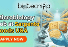Microbiology Job Opportunity in USA | Apply Today at Sargento Foods Microbiology Job Opportunity in USA Apply Today at Sargento Foods A professional featured image for a Microbiology Job at Sargento Foods USA. The design features the Biotecnika Global logo at the top center. On the right, a scientist in a lab coat and blue gloves holds a Petri dish, with a background showing shelves of aging cheese wheels and a microscope, symbolizing food microbiology. The left side displays the bold text "Microbiology Job at Sargento Foods USA" above a vibrant orange "APPLY NOW" button, all set against a clean, modern teal gradient background.