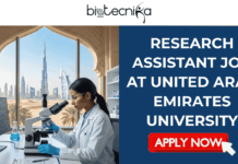 Research Assistant Job in UAE | United Arab Emirates University Hiring Now Research Assistant Job at United Arab Emirates University in UAE. A promotional banner for a "Research Assistant Job at United Arab Emirates University in UAE" posted by Biotecnika Global. The left side features a photo of a female scientist in a lab coat working with a microscope and computer, with a large arched window overlooking a modern UAE skyline in the background. The right side contains the job title text and an orange "APPLY NOW" button against a blue and gold gradient background.