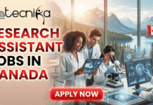 Research Assistant Jobs in Canada | Apply Now at University of Calgary Research Assistant Jobs at the University of Calgary, Canada. A featured image for a job advertisement titled "RESEARCH ASSISTANT JOBS IN CANADA" in bold red and white text. The graphic features a diverse group of three young researchers in white lab coats collaborating in a modern, high-tech laboratory. One researcher uses a microscope, while the others review data on a tablet and a large computer monitor displaying global research data. Through the expansive windows in the background, a breathtaking view of the Canadian Rockies and a pine forest is visible, with a Canadian flag prominently displayed. The Biotecnika Global logo is positioned in the top left corner, and a bright red "APPLY NOW" button is at the bottom center.