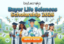 Scholarship in Hawaii for Life Science Students | Bayer Hawaii 2026 Application Invited Scholarship in Hawaii for Life Science Students Application Invited. A bright and inspiring promotional banner for the "Bayer Life Sciences Scholarship 2026" by Biotecnika Global. The illustration features a diverse group of smiling young scientists wearing both white lab coats and graduation caps, symbolizing academic and professional success. They are holding flasks and digital tablets in front of a modern research campus and a large globe. Scientific icons like DNA strands and microscopes float in the sky. A prominent orange "APPLY NOW" button is at the bottom center.