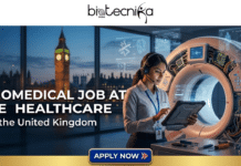 Urgent Hiring! High-Growth Biomedical Job at GE Healthcare in the UK You Shouldn’t Ignore High-Growth Biomedical Job at GE Healthcare in the UK. A promotional banner featuring the biotecnika Global logo at the top. The bold text on the left reads: "BIOMEDICAL JOB AT GE HEALTHCARE In the United Kingdom," followed by "Shape the Future of Advanced Healthcare Technology." On the right, a female engineer of diverse heritage, wearing a white lab coat, headset with a microphone, and an ID badge, uses a rugged tablet next to an open-cased GE medical imaging machine (CT/MRI scanner). The machine's complex internal components, circuit boards, and wires are exposed. Inside the exposed casing, a large Union Jack flag pattern is visible, alongside multiple transparent screens displaying medical diagnostic data and bone structure diagrams. Tools are laid out on a sterile lab bench in the foreground. The background is a large window with a panoramic view of the dusk London skyline, featuring an illuminated Elizabeth Tower (Big Ben) and the Houses of Parliament. At the bottom, a prominent blue and gold button reads "APPLY NOW" with a Union Jack flag icon