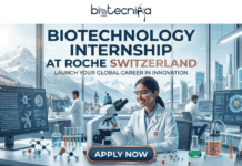 Biotechnology Internship in Switzerland | Roche Hiring Students Now! Biotechnology Internship in Switzerland Roche Hiring Students NOW. A promotional banner titled "BIOTECHNOLOGY INTERNSHIP AT ROCHE SWITZERLAND," featuring the "biotechnika Global" logo at the top center. The sub-headline reads: "LAUNCH YOUR GLOBAL CAREER IN INNOVATION." The image depicts a modern, high-tech biotechnology laboratory with large, floor-to-ceiling windows. A smiling diverse female scientist, her lab coat adorned with a Swiss flag pin, is sitting at a detailed lab desk, looking into a microscope. Her desk is covered with lab equipment like beakers of colorful liquids, flasks, molecular models, and digital monitors. One monitor prominently displays a detailed DNA double helix and cellular diagrams under the text "CELL THERAPY PLATFORM." Two male colleagues are visible working at other desks in the background. Through the massive windows, a dramatic, sun-drenched panorama of the snow-capped Swiss Alps and a modern city skyline is perfectly visible. A prominent, stylized golden-copper "APPLY NOW" button with an arrow is centered at the bottom. Small text at the bottom right reads: "#SwissBiotechCareer #ShapeTheFuture". The entire composition is detailed, clean-lined, and aspirational.