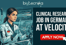 Hiring Now: Clinical Research Job in Germany at Velocity | Don’t Miss This Opportunity CLINICAL RESEARCH JOB IN GERMANY AT VELOCITY. An illustrated banner features a woman with dark hair in a white lab coat working in a modern, high-tech laboratory filled with micropipettes, robotic arms, and computer screens. She holds an electronic pipette in one hand and points at a glowing molecular structure on a transparent tablet. The top has a logo banner that reads "biotecnika Global". The right side features large white text stating "CLINICAL RESEARCH JOB IN GERMANY AT VELOCITY," with a rounded call-to-action button below it that reads "APPLY NOW" against an orange-to-teal gradient.