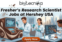 Dream Research Scientist Role at Hershey USA – High-Paying Jobs in USA for Freshers! Dream Research Scientist Role at Hershey USA – High-Paying Jobs in USA for Freshers! An innovative and engaging featured image for a job page. At the top, a clean header banner with the biotecnika Global logo (text, globe, and figure) and a stylized rocket trail. Below it, large text reads: "Fresher's Research Scientist Jobs at Hershey USA". Below this banner is a dynamic illustrative scene of a futuristic, chocolate-themed food science laboratory. Three diverse young scientists in lab coats are actively engaged. On the left, a man works with a custom brown research console featuring a screen labeled "Flavour Profile Research" and showing nodes on a USA map. In the center, a woman smiles, holding a beaker with a green sample (like cocoa leaves) and examining another in a flask. On the right, a man interacts with a large computer screen displaying a complex molecular model. Jars of cocoa beans, beakers of colored liquids, and modern equipment fill the lab. At the bottom center, a prominent orange button with white text and a pointer says: "Apply Now". The entire composition is vibrant, forward-looking, and designed to attract aspiring scientists to a career in global research and innovation. No Hershey company logo is added. The style is modern digital illustration.