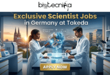 Exclusive Scientist Jobs in Germany | Takeda Hiring Now Exclusive Scientist Jobs in Germany Takeda Hiring Now. A promotional featured image for Biotecnika Global advertising exclusive scientist jobs in Germany at Takeda. The image shows two scientists (one woman and one man) in a high-tech laboratory with large windows overlooking the Cologne Cathedral and city skyline at sunset. They are interacting with a 3D holographic projection of a complex protein structure with an 'Exclusive Access to Target ID' label and the Takeda logo. The lab is equipped with modern research tools, microscopes, and labeled equipment like a bioreactor with a plaque for 'Deutschland R&D Excellence.' A prominent gold 'APPLY NOW' button is at the bottom, and the biotecnika Global logo is at the top. The overall style is modern, professional, and aspirational.