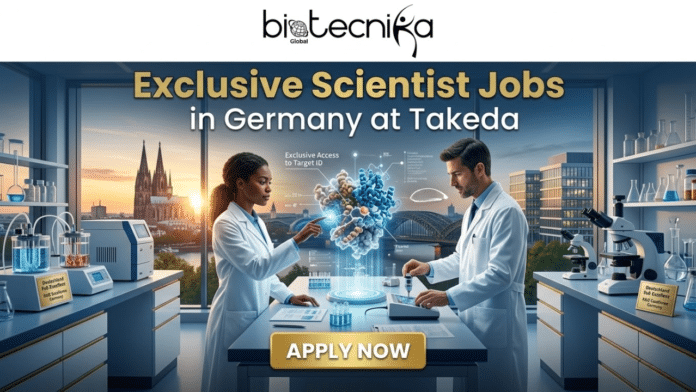 Exclusive Scientist Jobs in Germany Takeda Hiring Now. A promotional featured image for Biotecnika Global advertising exclusive scientist jobs in Germany at Takeda. The image shows two scientists (one woman and one man) in a high-tech laboratory with large windows overlooking the Cologne Cathedral and city skyline at sunset. They are interacting with a 3D holographic projection of a complex protein structure with an 'Exclusive Access to Target ID' label and the Takeda logo. The lab is equipped with modern research tools, microscopes, and labeled equipment like a bioreactor with a plaque for 'Deutschland R&D Excellence.' A prominent gold 'APPLY NOW' button is at the bottom, and the biotecnika Global logo is at the top. The overall style is modern, professional, and aspirational.