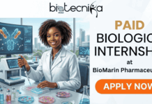 Paid Internship in USA | Apply For Biologics Intern at BioMarin Pharmaceutical Paid Internship at BioMarin Pharmaceutical USA | Don't Miss It. A high-quality featured banner image for a job page, split between an illustration on the left and text on the right, with a logo banner across the top. The top light grey header features the centered black 'biotecnika Global' logo, which includes stylized 'biotecnika' text, a globe icon with 'Global' below it, and a stylized dancing figure to the right. The left section (60% width) is a detailed, dynamic illustration of a smiling young Black woman with coily hair, wearing a white lab coat. She is seated at a high-tech laboratory workbench, actively using a micropipette to transfer liquid into a multi-well plate. Behind her, a large monitor displays a complex, colourful 3D molecular model of an antibody and scientific charts, with a small 'biotecnika Global' logo. Various laboratory equipment like a large bioreactor vessel with orange liquid, glass vials, and petri dishes with cultures are on the bench. Through a large window, a modern biotechnology park city skyline is visible. The right section (40% width) has a clean, light background with prominent text stacked and arranged: "PAID" (large, gold font), followed by "BIOLOGICS INTERNSHIP" (large, black font), then "at" and "BioMarin Pharmaceutical" (clear, black text). At the bottom right of the text area, a large, rounded orange button contains the bold white text "APPLY NOW". The overall composition is professional, engaging, and designed to be attention-grabbing, with no BioMarin Pharmaceutical logo present, only text.