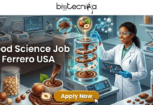 Urgent Hiring: Food Science Job in USA – Night Shift Quality Technician at Ferrero You Can’t Miss! Food Science Job in USA Quality Technician Ferrero Jobs. A detailed, dynamic infographic header image for a job posting. At the top center, the complete black 'biotecnika Global' logo (with text, globe, and dynamic human figure) is positioned against a textured white bar. Below it, large, bold white sans-serif text across the center reads: 'Food Science Job at Ferrero USA'. The central area features a vibrant, rich, and high-tech food science laboratory scene focused on chocolate innovation. A futuristic, glass-walled processing machine with an internal, glowing spiral processes a swirling mixture of chocolate and hazelnut cream, creating a unique visual pattern. The lab is filled with sophisticated equipment, including multiple high-speed centrifuges with analytical screens displaying data plots, complex analytical screens, bioreactor-like processing machines, a vacuum sealer for product prototyping, jars of raw ingredients like cocoa beans and various types of hazelnuts (unshelled and shelled), and a bowl of melted chocolate with a stylized swirl and perfect whole hazelnuts. Stylized, glowing molecular models of flavor and ingredient structures float in the air, along with analytical data visualizations. The entire composition is visually rich, with a deep chocolate brown, gold, and hazelnut beige color palette highlighted by scientific blues and greens. Depth of field is present, making the lab feel active and modern. At the bottom center, a prominent, polished, button-shaped element (colored in a rich gold-orange that pops) contains the clear, bold text 'Apply Now' in white font, with a subtle mouse pointer indicating a click. The overall lighting is focused and clean, giving the scene an optimistic and innovative feel.