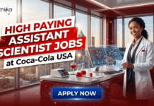 High Paying Assistant Scientist Jobs at Coca-Cola USA | Food Science Graduates Shouldn’t Miss This! High Paying Assistant Scientist Jobs at Coca-Cola USA Food Science Graduates Shouldn’t Miss This!. A professional promotional graphic with the "Biotecnika GLOBAL" logo in the top-left corner. The central headline is a large, stacked red and white text block that reads, "HIGH PAYING ASSISTANT SCIENTIST JOBS" with "at Coca-Cola USA" in black text below. On the right, a smiling Black woman scientist with confident expression, wearing a white lab coat over professional attire, points at a large computer monitor displaying a dynamic molecular model. She stands in a modern, red-themed laboratory with a desk full of lab equipment and a large window looking out onto a modern city skyline at dusk. At the bottom center, a glowing blue "APPLY NOW" button is prominently displayed.