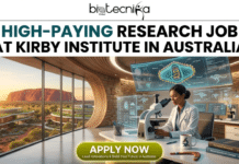 High-Paying Research Job in Australia – Join Kirby Institute as a Research Officer Today! High-Paying Research Job in Australia – Join Kirby Institute as a Research Officer Today! An informative featured image banner for a high-paying research job at the Kirby Institute in Australia. At the top center, the biotechnika Global logo is displayed above large, bold text reading: 'HIGH-PAYING RESEARCH JOB AT KIRBY INSTITUTE IN AUSTRALIA'. The banner shows a female researcher in a lab coat looking into a microscope in a futuristic office with massive, curved windows. Through the windows, a dramatic sunset view of Uluru (Ayers Rock) in the Australian outback is visible, with modern, green-roofed buildings nearby. Multiple computer screens display detailed scientific data and a 3D model of a labeled virus (retrovirus, suitable for Kirby Institute focus) with miniature kangaroo and koala figures. On her desk are more microscopes, textbooks, and a boomerang-shaped pen holder with a koala figure. A prominent yellow 'APPLY NOW' button is at the bottom center, with smaller text below reading: 'Lead Innovations & Build Your Future in Australia.' and 'PREMIUM BRANDS, NO COMPANY'. The entire composition is visually rich and captures the unique theme.