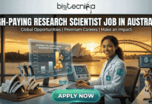 High-Paying Research Scientist Job in Australia – Earn Upto $96,073 High-Paying Research Scientist Job in Australia Earn Upto $96K. An advertisement for a "High-Paying Research Scientist Job in Australia" featuring a smiling female scientist in a lab coat. She sits at a futuristic desk with a holographic screen displaying a bar chart of "GLOBAL VS. AUSTRALIAN SCIENTIST SALARIES", with Australian salaries higher. A stack of coins sits at the base of the chart. The background window overlooks the Sydney Opera House and Harbour Bridge at sunset. Miniature models of the Opera House and Harbour Bridge, along with lab pipettes and a kangaroo wearing a lab collar, are on the desk. The biotecnika Global logo is at the top center. A green "APPLY NOW" button with a bright glow is at the bottom center. Sub-headline: "Global Opportunities | Premium Careers | Make an Impact".