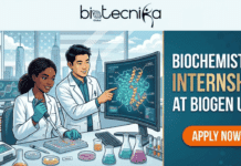 Paid Biochemistry Internship in the USA | Apply For Analytical Development Co-op at Biogen Paid Biochemistry Internship at Biogen USA Apply Now. An illustrated split-screen banner with a top logo centered that reads "biotecnika Global". The left side shows a detailed cartoon laboratory setting where a Black woman in a lab coat and blue gloves uses a micropipette to work with a multi-well plate, while an Asian man in a lab coat points to a large monitor displaying a complex 3D protein structure. The background features a city skyline resembling New York through the window, an American flag, and lab equipment like beakers with colorful liquids. The right side is a dark teal panel with gold and white text: "BIOCHEMISTRY INTERNSHIP AT BIOGEN USA" above a large orange button that says "APPLY NOW".