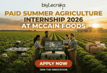 Paid Summer Agriculture Internship 2026 | McCain Foods Hiring Biology & Agriculture Students! Paid Summer Agriculture Internship 2026 at McCain Foods. A promotional banner for biotecnika Global promoting a 'Paid Summer Agriculture Internship 2026 at McCain Foods'. The central image is a diverse group of four enthusiastic young adults (an African American man and woman, and two Caucasian individuals) standing in a lush green row crop field at a warm sunset. They are clustered around a large interactive touchscreen monitor displaying complex agricultural data visualizations and maps. To their left, a professional drone is on a landing pad, and other small field sensors are visible. To their right are crates of unbranded raw potatoes and generic packaging materials. In the background, a large modern agricultural building is silhouetted against the golden sunset sky. Large gold and white text at the top center reads: 'PAID SUMMER AGRICULTURE INTERNSHIP 2026 AT MCCAIN FOODS'. A large prominent 'APPLY NOW' button in a contrasting color is at the bottom center. Below the main group, text says 'JOIN THE INNOVATION'. The biotecnika Global logo is prominent at the top of the image. The entire scene blends modern technology with agriculture.