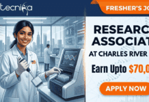 Research Associate Freshers Job at Charles River USA | Life Science Candidates Earn Upto $70,000 Research Associate Job at Charles River USA Fresher's Job. A split featured image job posting graphic. The top header features the 'biotecnika Global' logo on the left and an orange 'FRESHER’S JOB' banner on the right. The left panel is a photograph of a smiling young South Asian woman scientist in a white lab coat with safety glasses, using a multichannel pipette, in a modern, glass-walled laboratory with other scientists and a USA flag pin on her lapel, and a view of a US city skyline. In the foreground is a DNA analysis machine with a screen showing a DNA double helix and a graph. The right panel contains bold text: 'RESEARCH ASSOCIATE', 'at Charles River USA', 'Earn Upto $70,000', with a large orange 'APPLY NOW' button below. The right background has subtle molecular patterns.