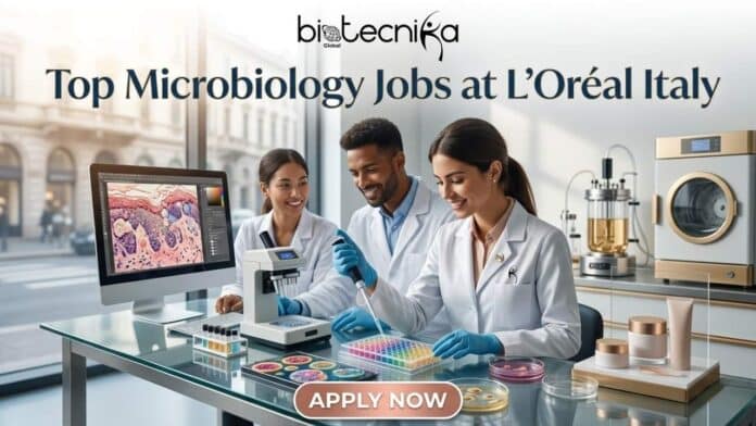 Top Microbiology Jobs in Italy L’Oréal Hiring Laboratory Technicians Now. A professional featured image for 'Top Microbiology Jobs at L’Oréal Italy' featuring the Biotecnika Global logo. The scene shows three diverse scientists in white lab coats collaborating in a modern, sunlit laboratory with high-tech equipment and skincare products. A prominent 'APPLY NOW' button is positioned at the bottom.