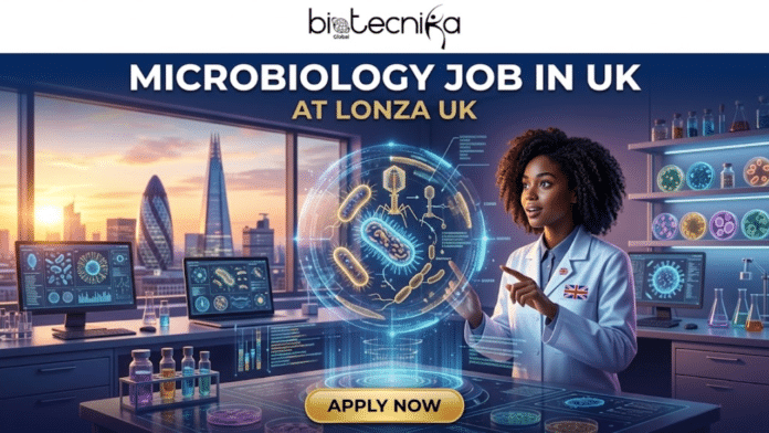 Latest Microbiology Job in UK at Lonza Life Science Graduates Are Eligible. A wide, detailed promotional job banner for biotecnika Global, featuring a futuristic, high-tech microbiology laboratory set against the London, UK skyline at dusk. At the top, the biotecnika logo with Global text is centered on a deep blue banner. Below it, the large, prominent headline text reads: MICROBIOLOGY JOB IN UK in white, with AT LONZA UK in smaller gold text below. The central figure is a young, curly-haired Black female scientist in a white lab coat with Union Jack flag pins, looking with focused intent and pointing at a massive, intricate 3D holographic projection. The projection displays a complex array of diverse microorganisms (including bacteria, viruses, and phages) with underlying data streams and grid patterns. To her left, a large window reveals the iconic London cityscape (including the Shard and Gherkin), with multiple computer monitors displaying detailed scientific data. To her right, shelves and a wall are filled with various glowing petri dishes and flasks, along with more monitors and a range of colored vials and equipment on the desk. At the very bottom, a large gold-colored button with text reads: APPLY NOW. The entire scene blends real physical objects with glowing digital interfaces and data, creating a scroll-stopping, viral, unique, and relatable visual for a high-level research position.